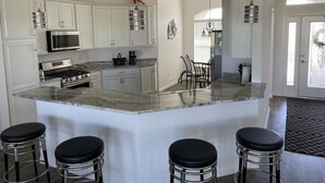 A modern kitchen with white cabinets, a large island with bar stools, stainless steel appliances, and decorative bird sculptures.