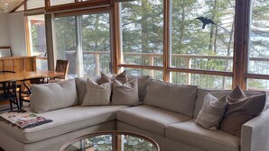 Ein geräumiges Wohnzimmer mit einer großen Eckcouch, einem Glastisch und Blick ins Freie durch große Fenster.