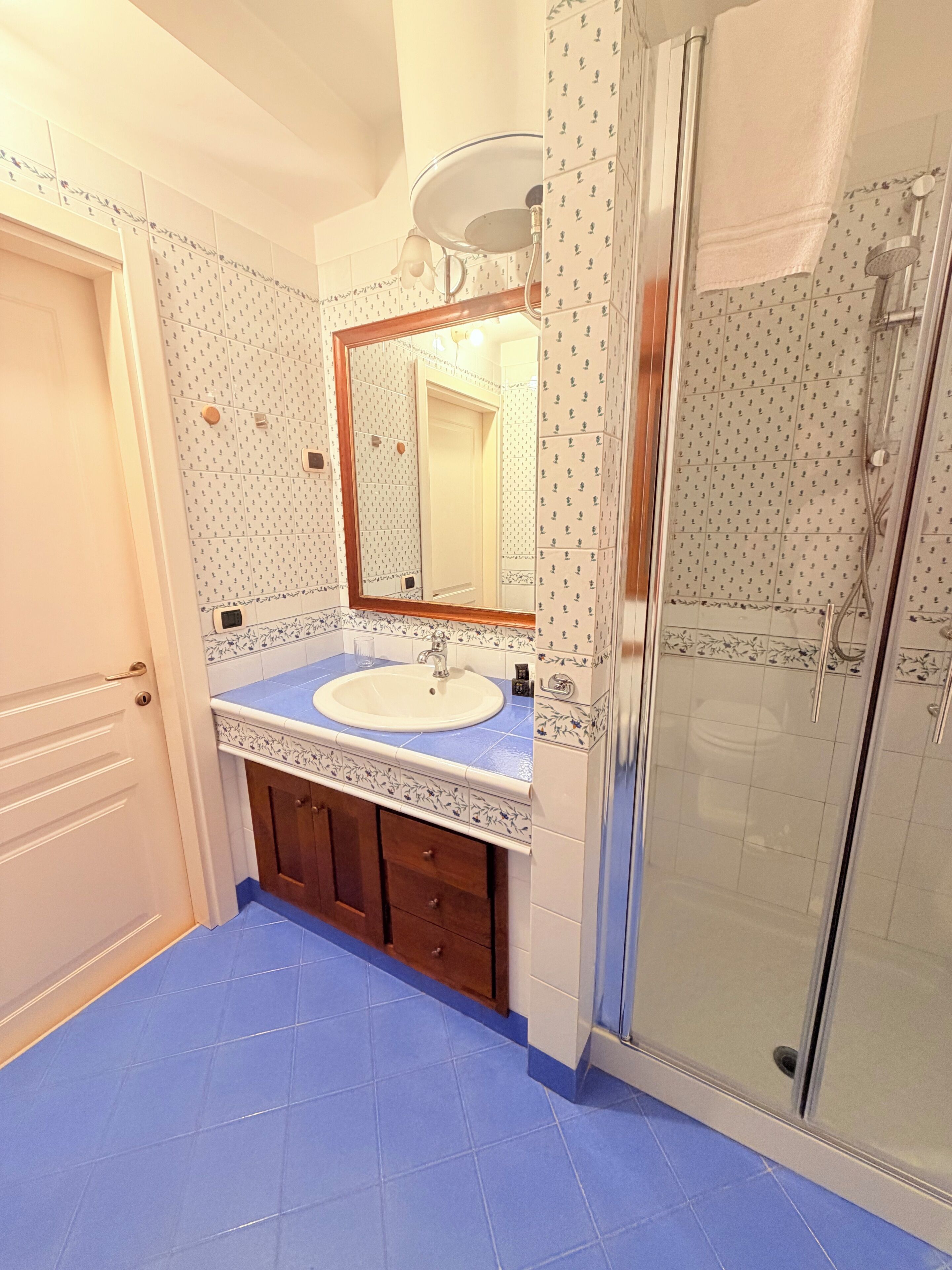 A bathroom with a sink, mirror, shower, and blue-tiled floor.