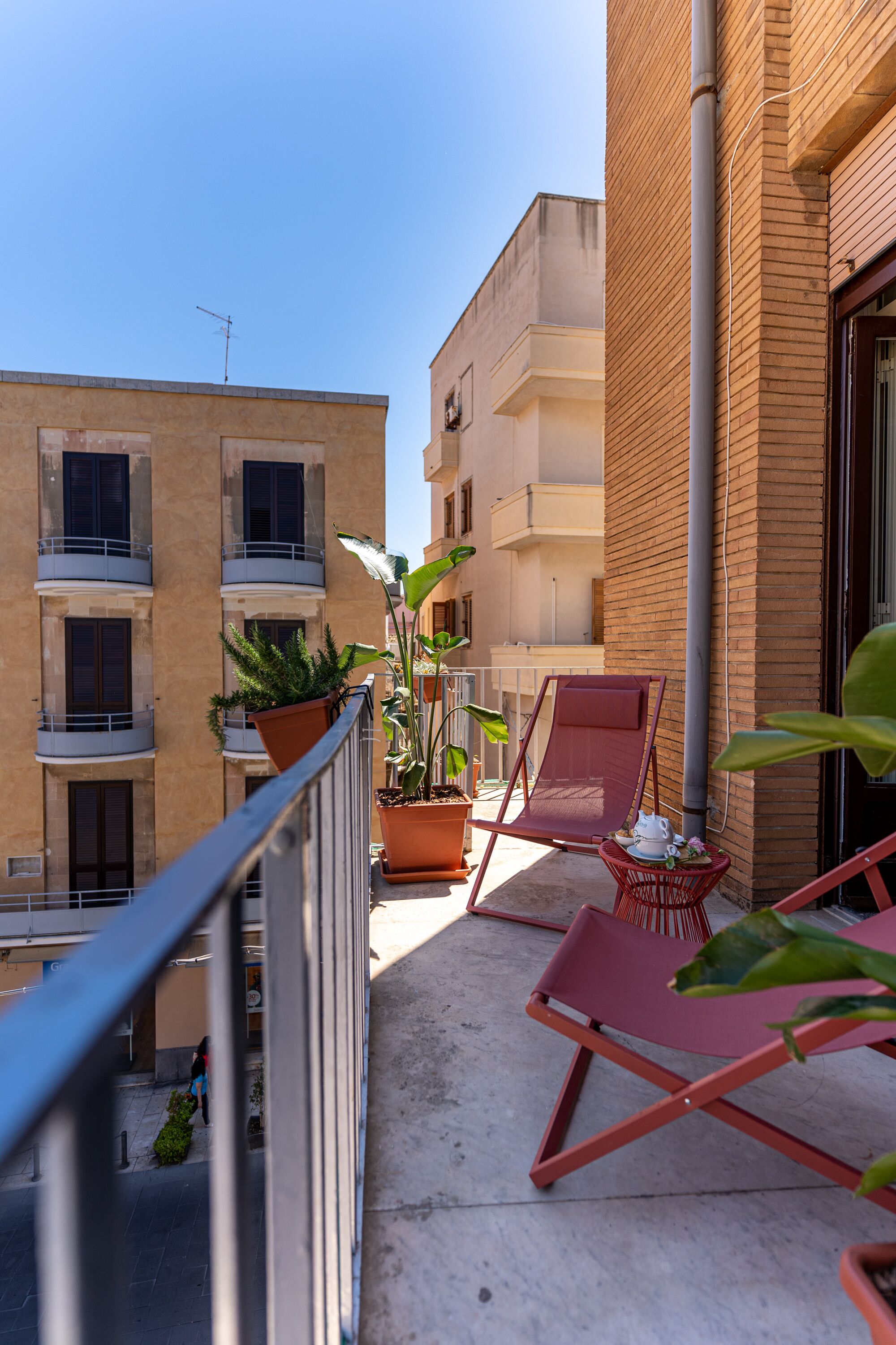 A balcony with potted plants, a red chair, and a small table.