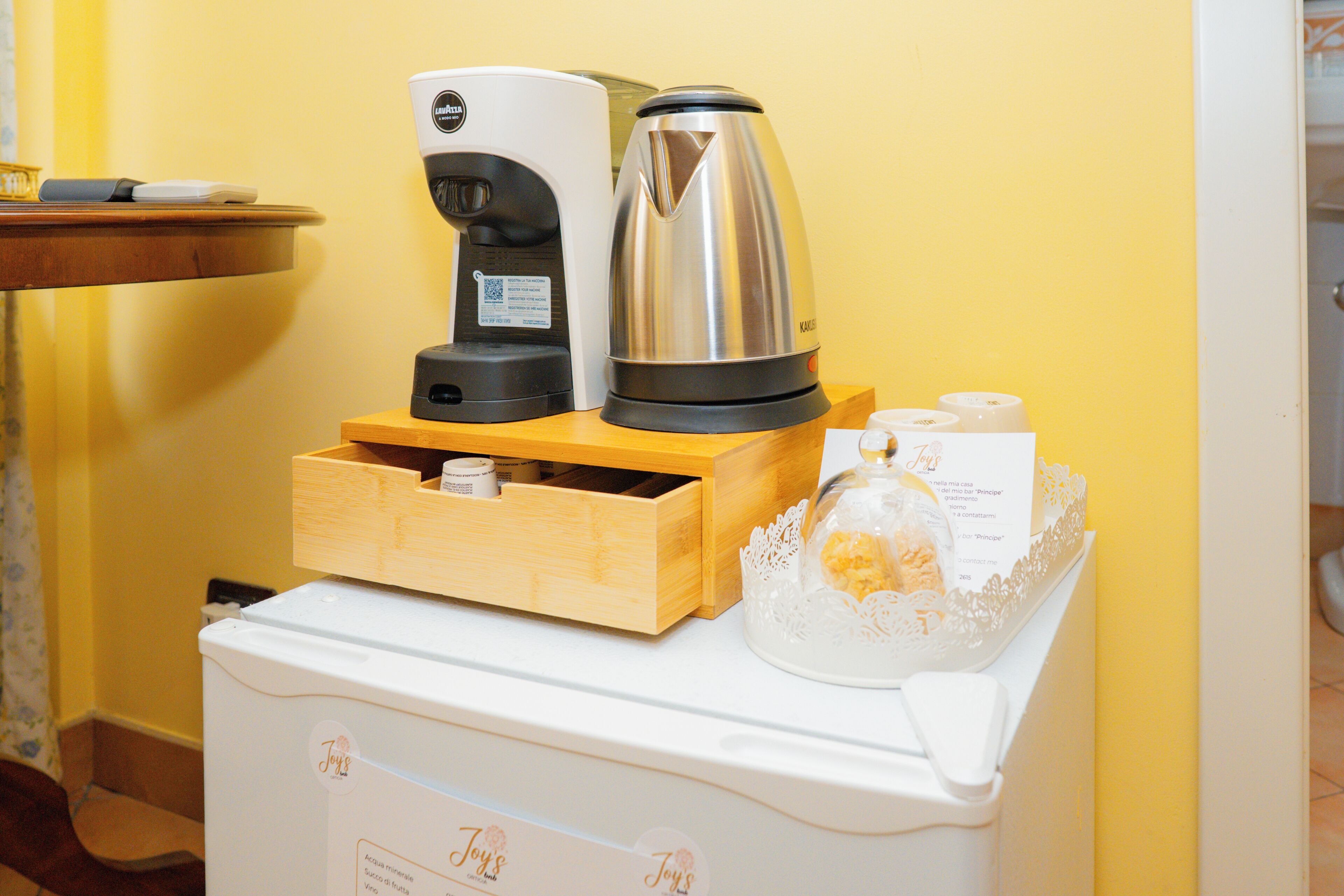 A kitchenette with a coffee maker, a kettle, and a small refrigerator.