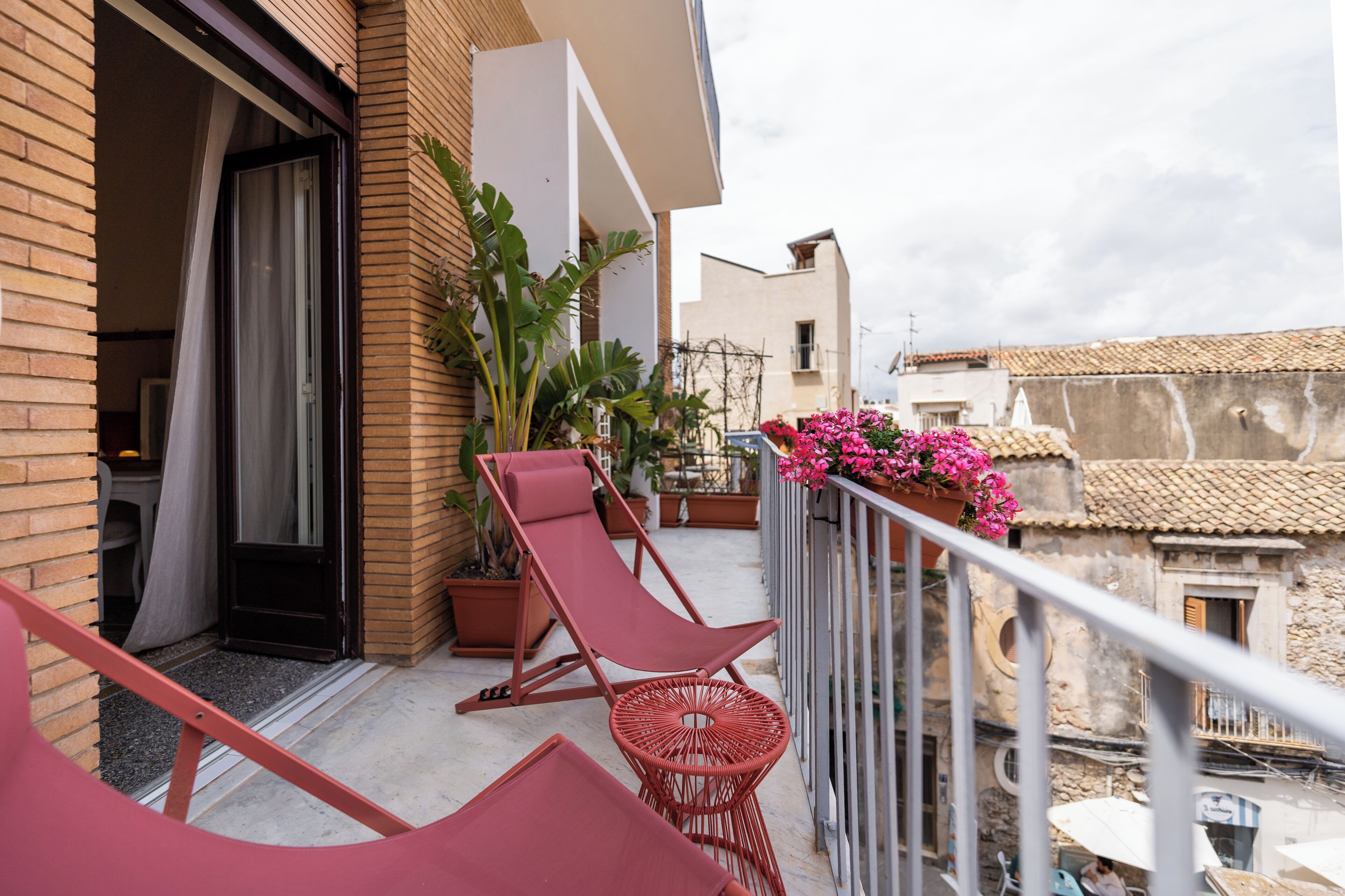 Ein Balkon mit roten Stühlen, einem Blumentopf und Blick auf benachbarte Gebäude.