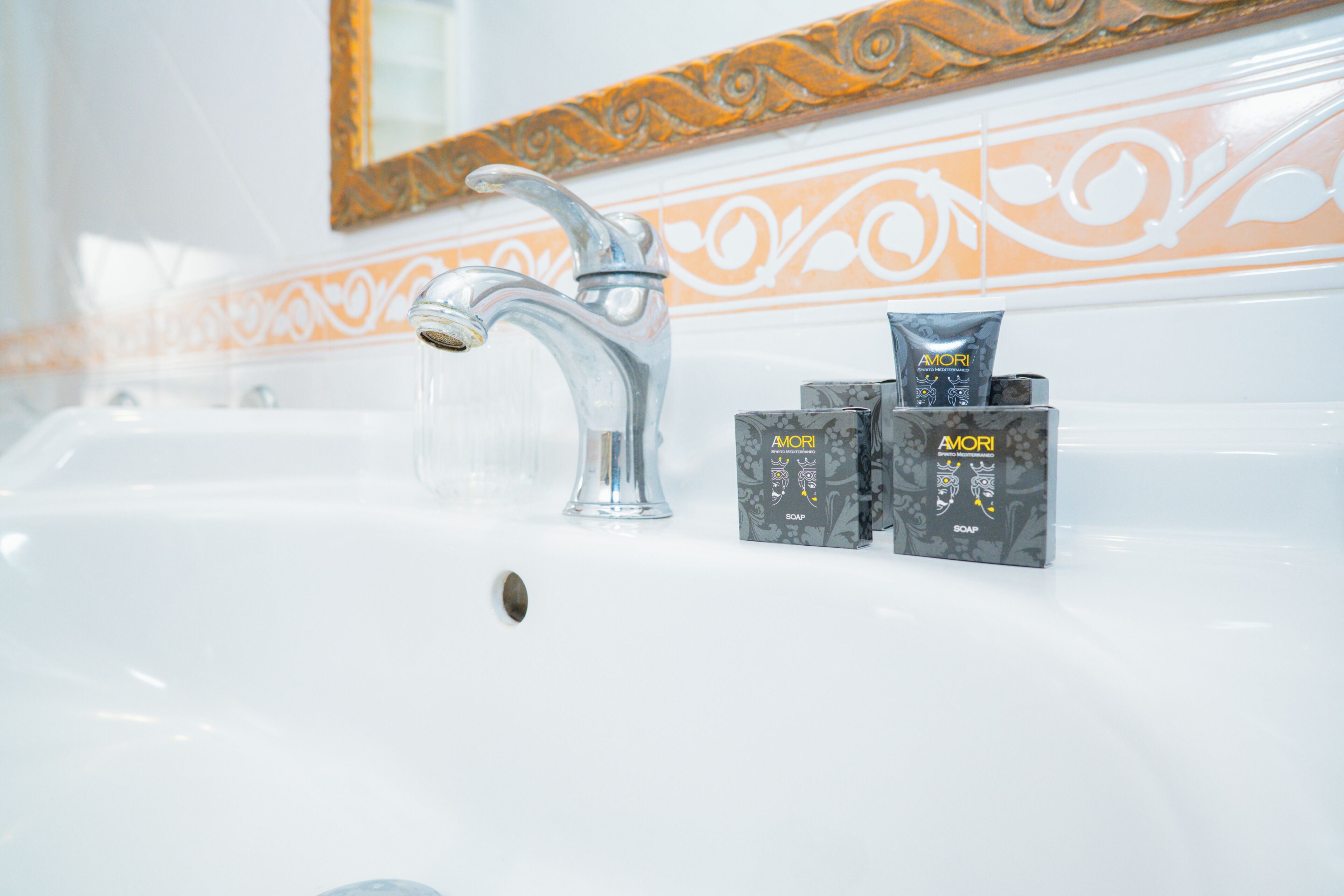 A bathroom sink with a modern faucet, a decorative mirror, and three soap dispensers.