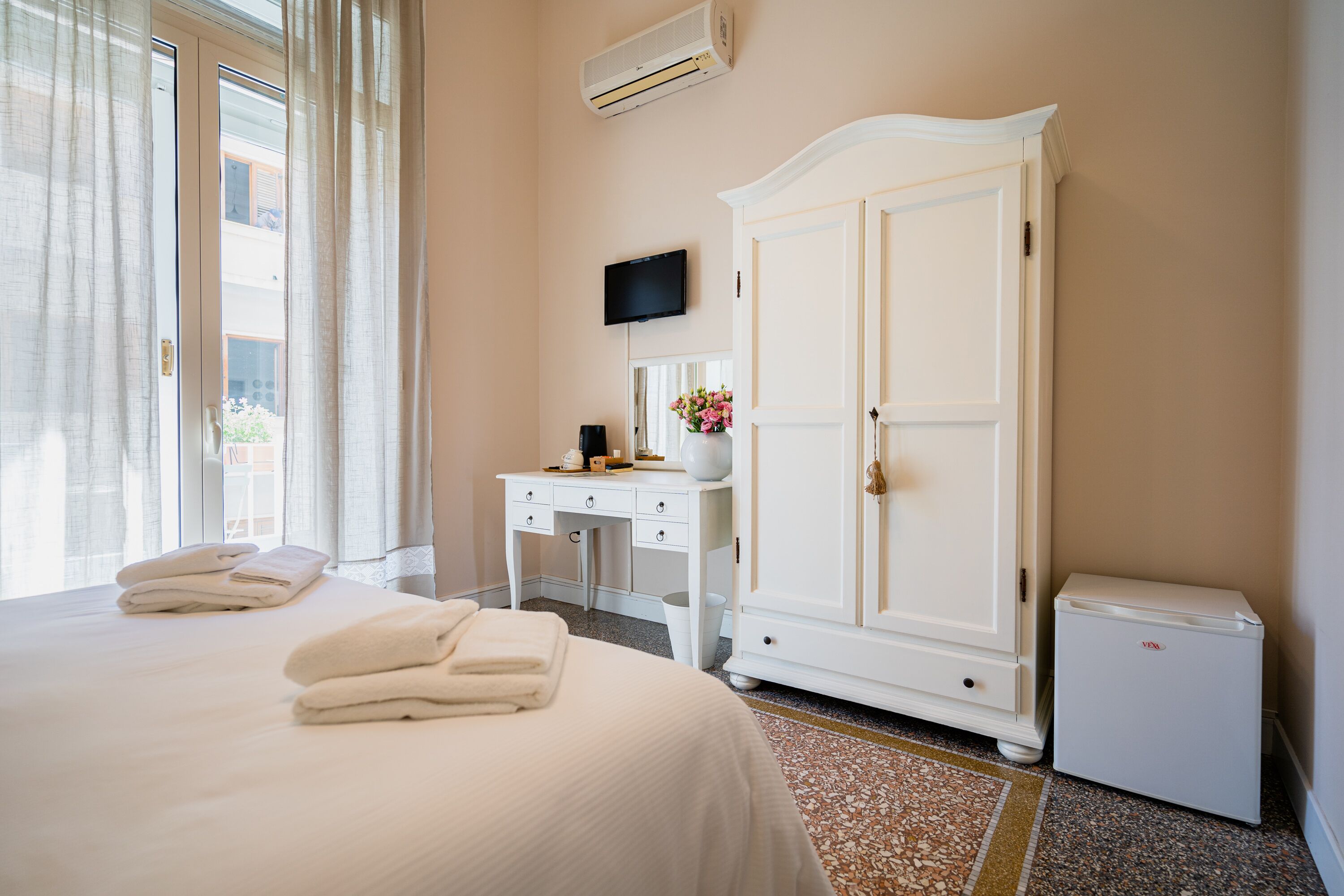 Une chambre d’hôtel équipée d’un lit, d’un bureau, d’une armoire, d’une télévision et d’un petit réfrigérateur.