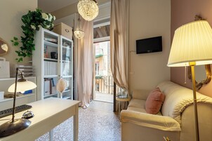 Una sala de estar con un sofá, un escritorio con una lámpara, un televisor y una estantería.