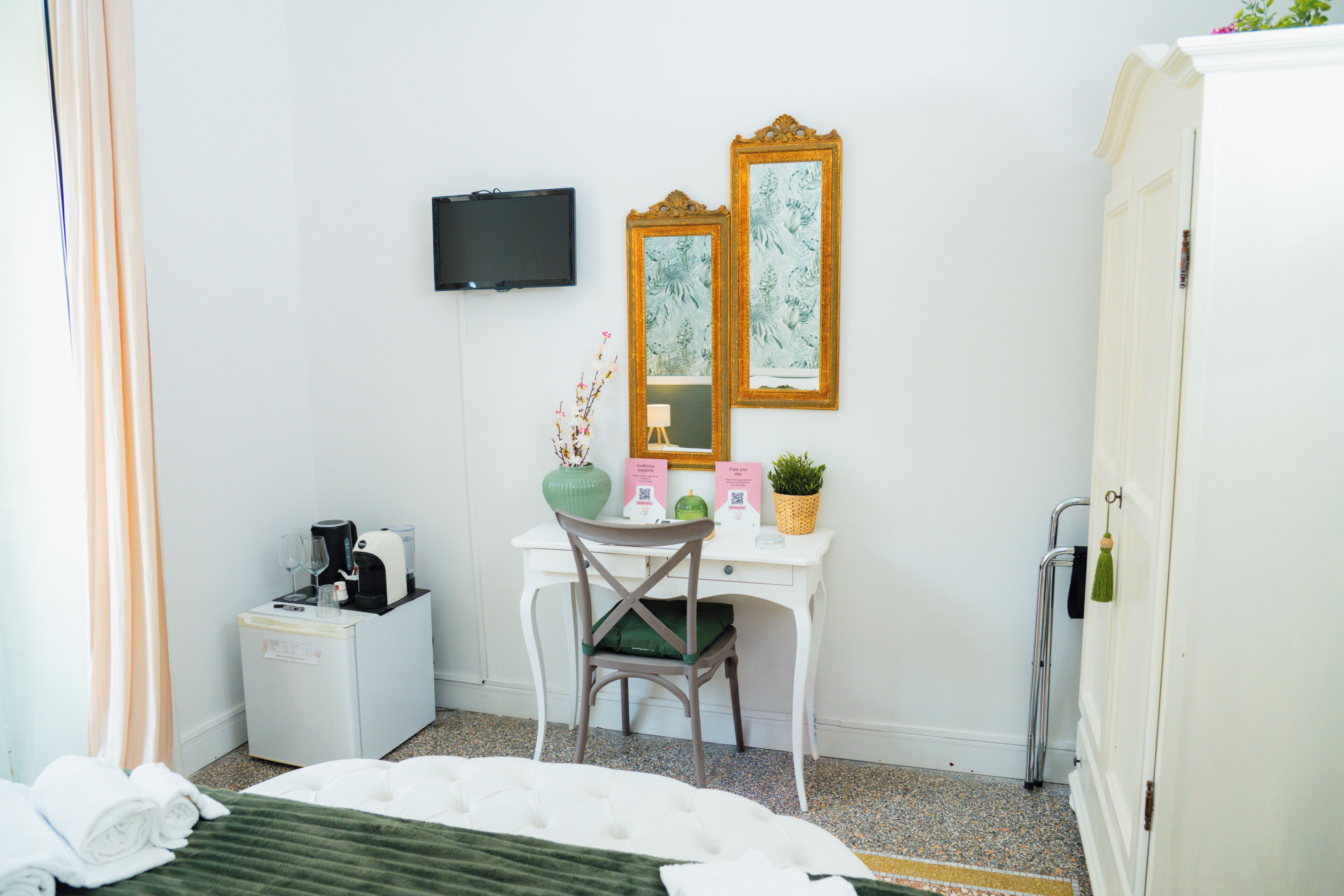 A hotel room with a bed, a desk with a chair, a television, a small refrigerator, and a mirror.