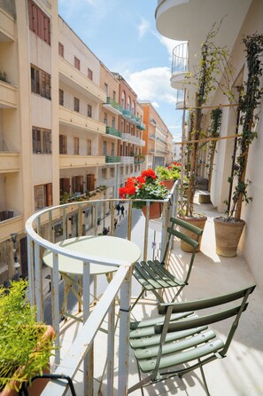 A balcony with a table and chairs, potted plants, and a view of adjacent buildings. - Joy's BnB Ortigia (Syracuse)