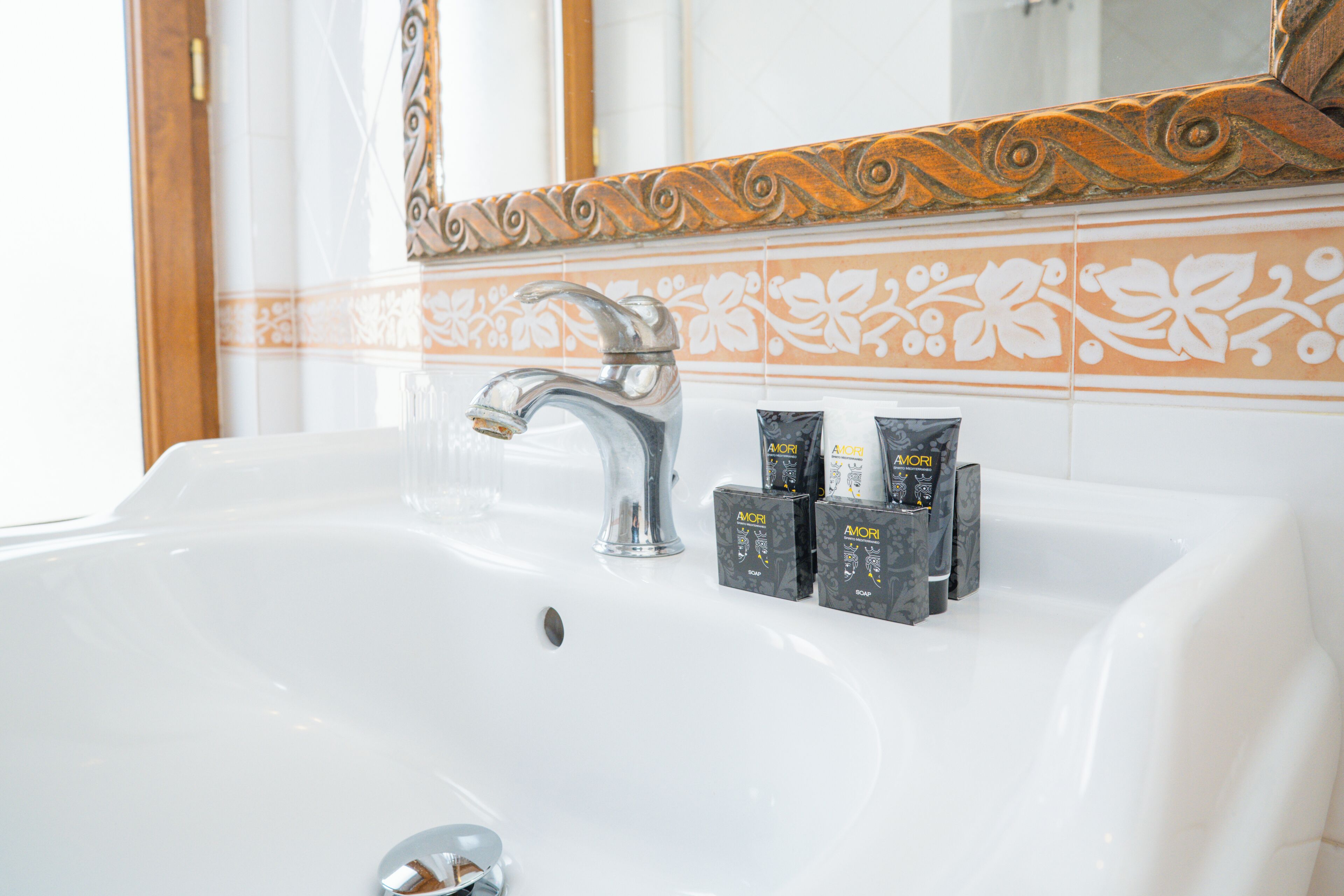 A bathroom sink with a mirror, decorative tiles, and toiletries.