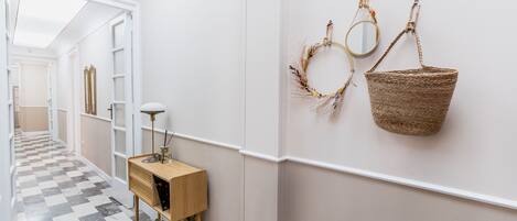 A hallway with a checkered floor, a wooden console table with a lamp, and wall-mounted mirrors and baskets.