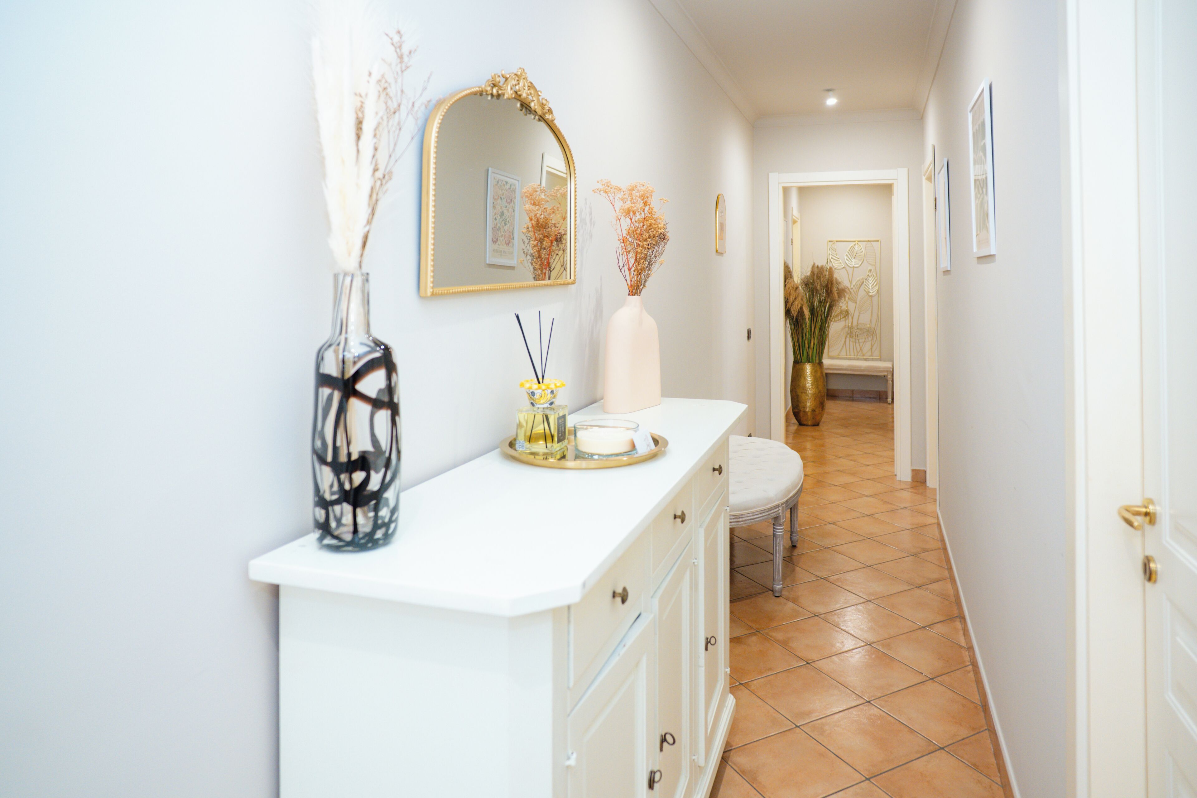 A hallway with a white console table, a mirror, and a vase with dried flowers.