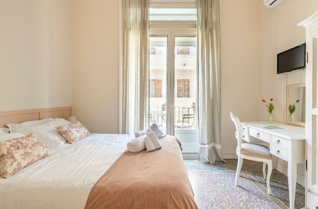 A hotel room with a bed, a desk, a chair, a television, and a view of the outside balcony.