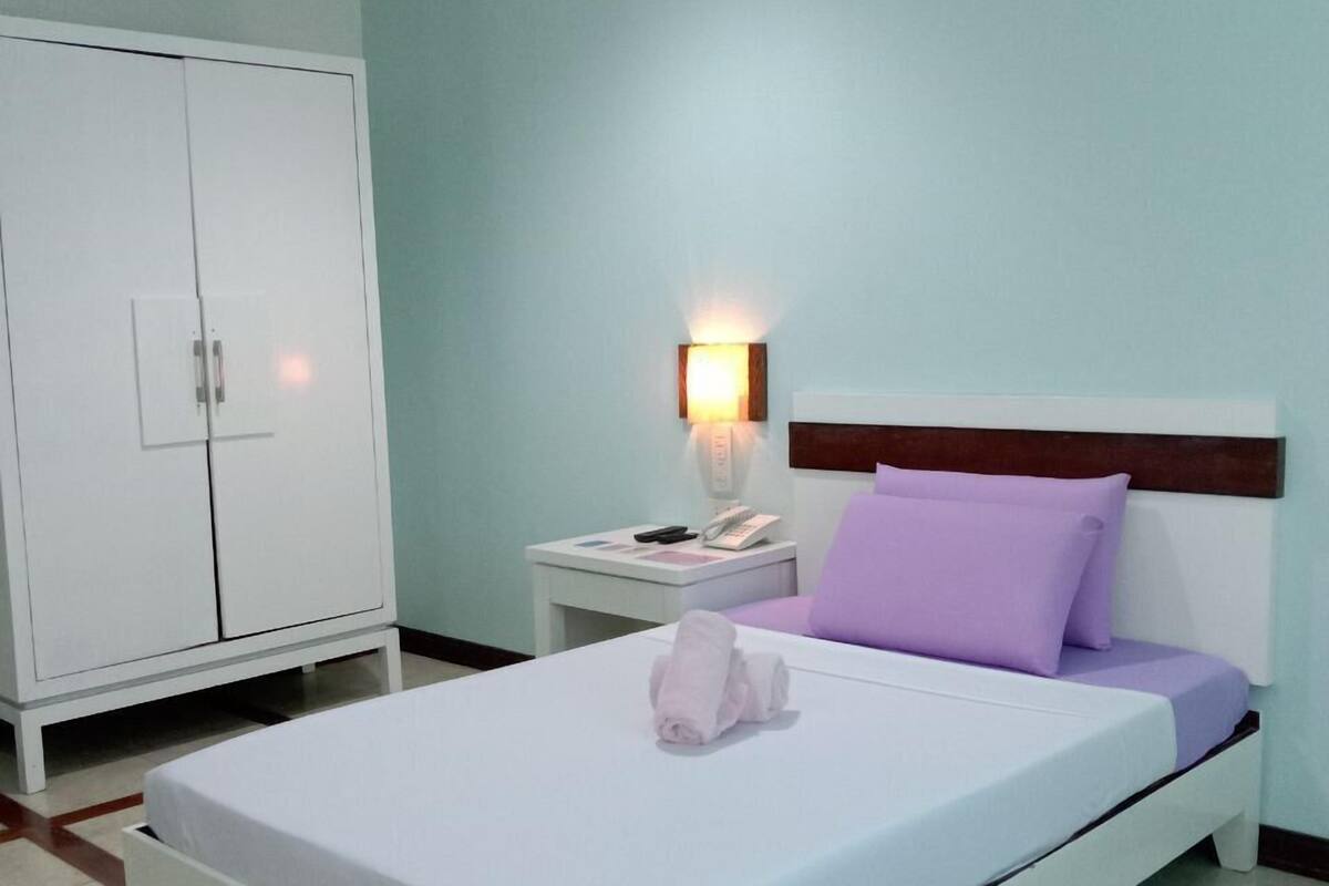 Ein ordentlich eingerichtetes Schlafzimmer mit einem Bett, einem Kleiderschrank, einem Nachttisch mit Lampe und Wandleuchte.