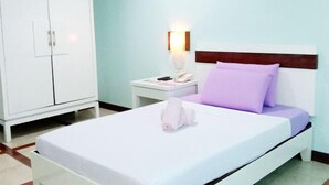 Una habitación de hotel con una cama blanca, una mesita de noche con lámpara y un armario.