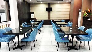 Una sala de conferencias con varias mesas y sillas, un televisor de pantalla plana montado en la pared, y una planta en maceta a la derecha.