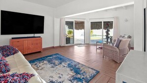 Ein geräumiges Wohnzimmer mit Flachbildfernseher, Holzschrank, Sofa, Korbstuhl und Esstisch.