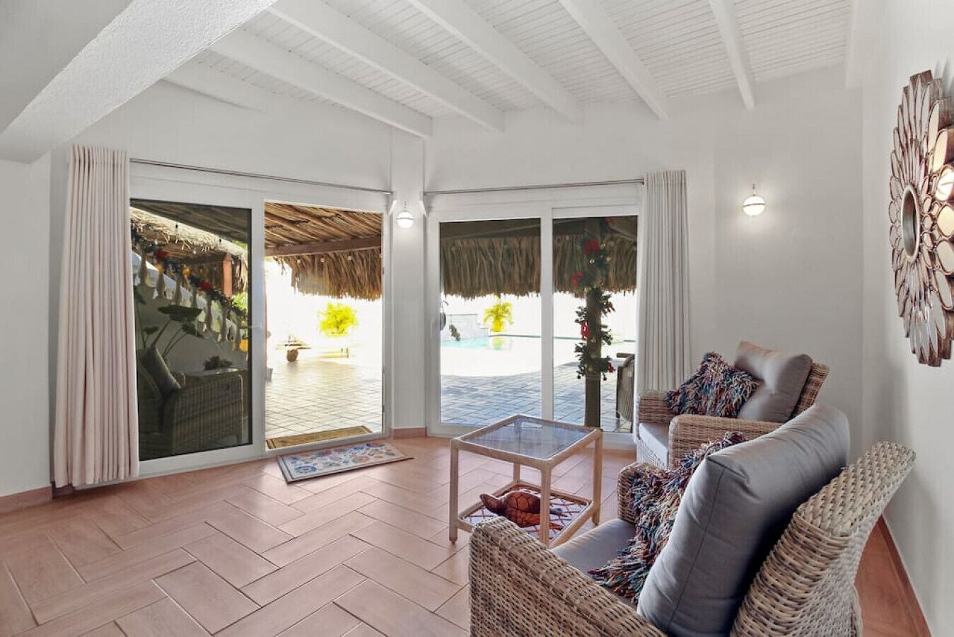 A spacious living area with a large sliding glass door leading to a poolside area, wicker furniture, and a decorative wall piece.