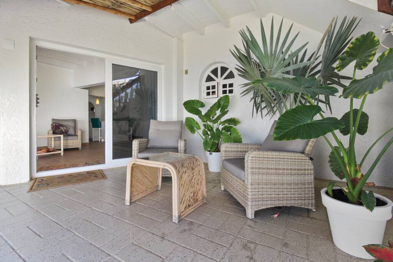 Un espace extérieur aménagé, abrité et doté de meubles en osier, de plantes en pot et d’une porte-fenêtre coulissante donnant accès à un espace intérieur.