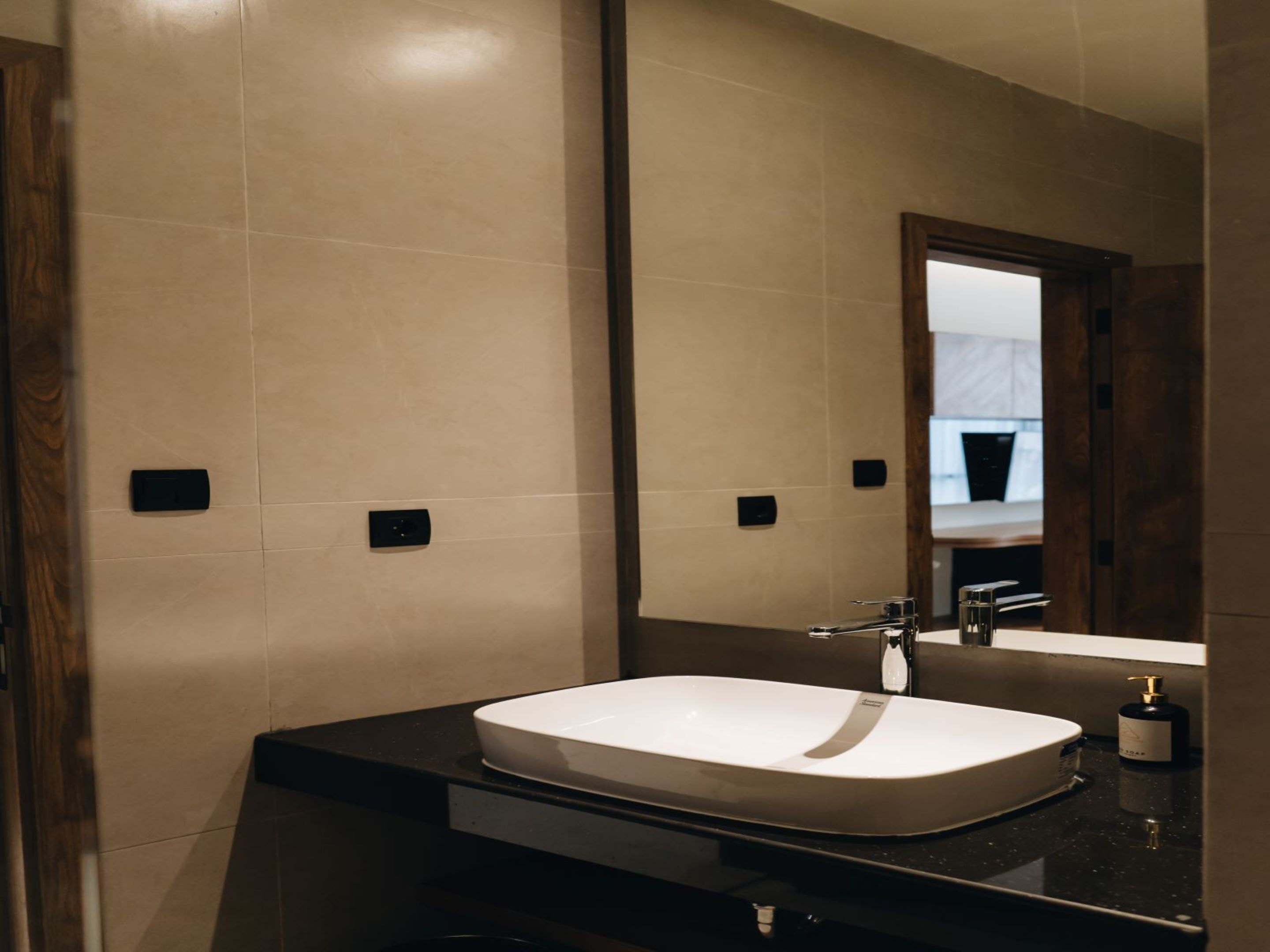 A modern bathroom with a large mirror, a white sink, and a dark countertop.