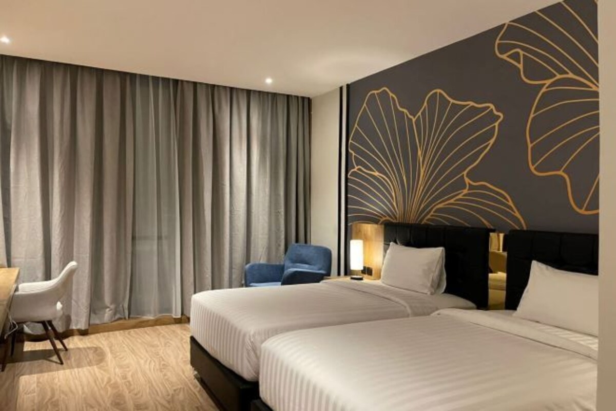 Habitación de hotel con dos camas, un escritorio, una silla y un amplio panel decorativo.