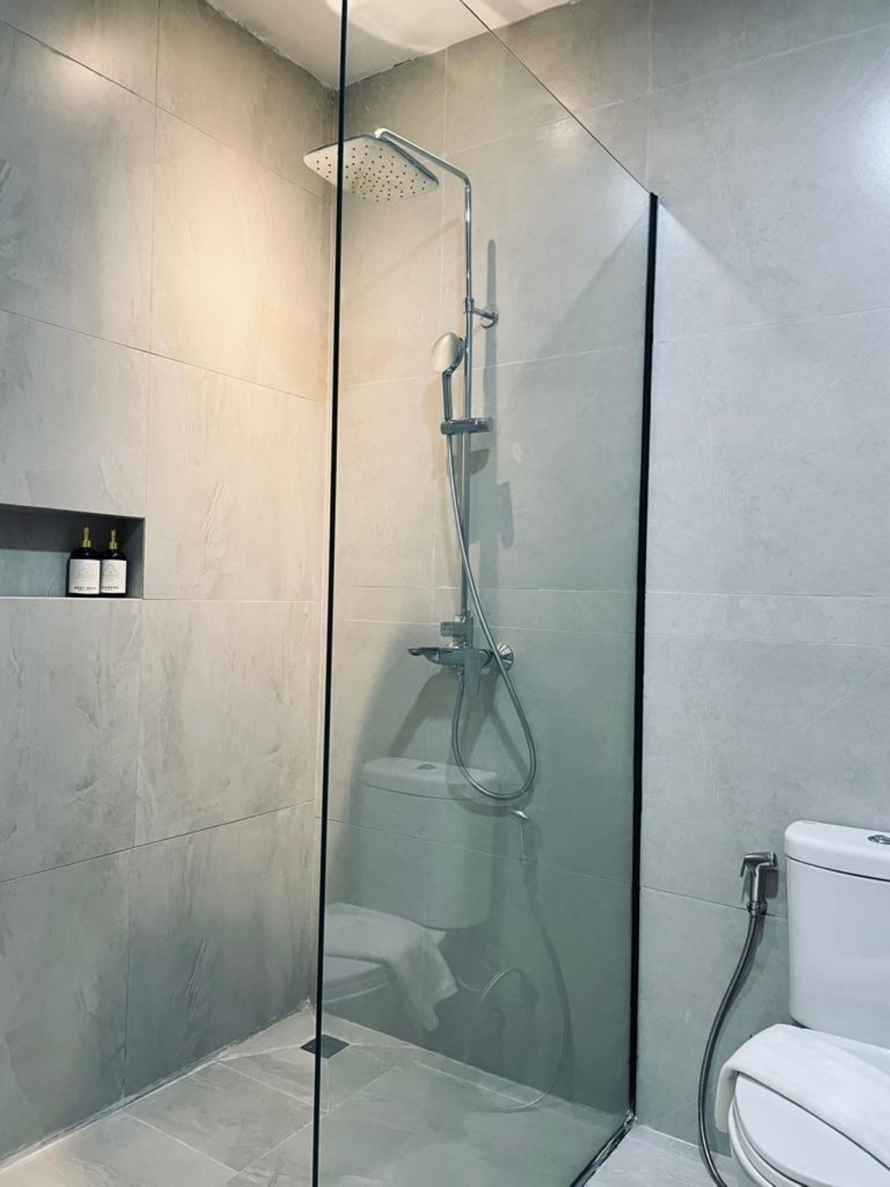 Een moderne badkamer met een douche met glazen wand, een toilet en een plank met flesjes.