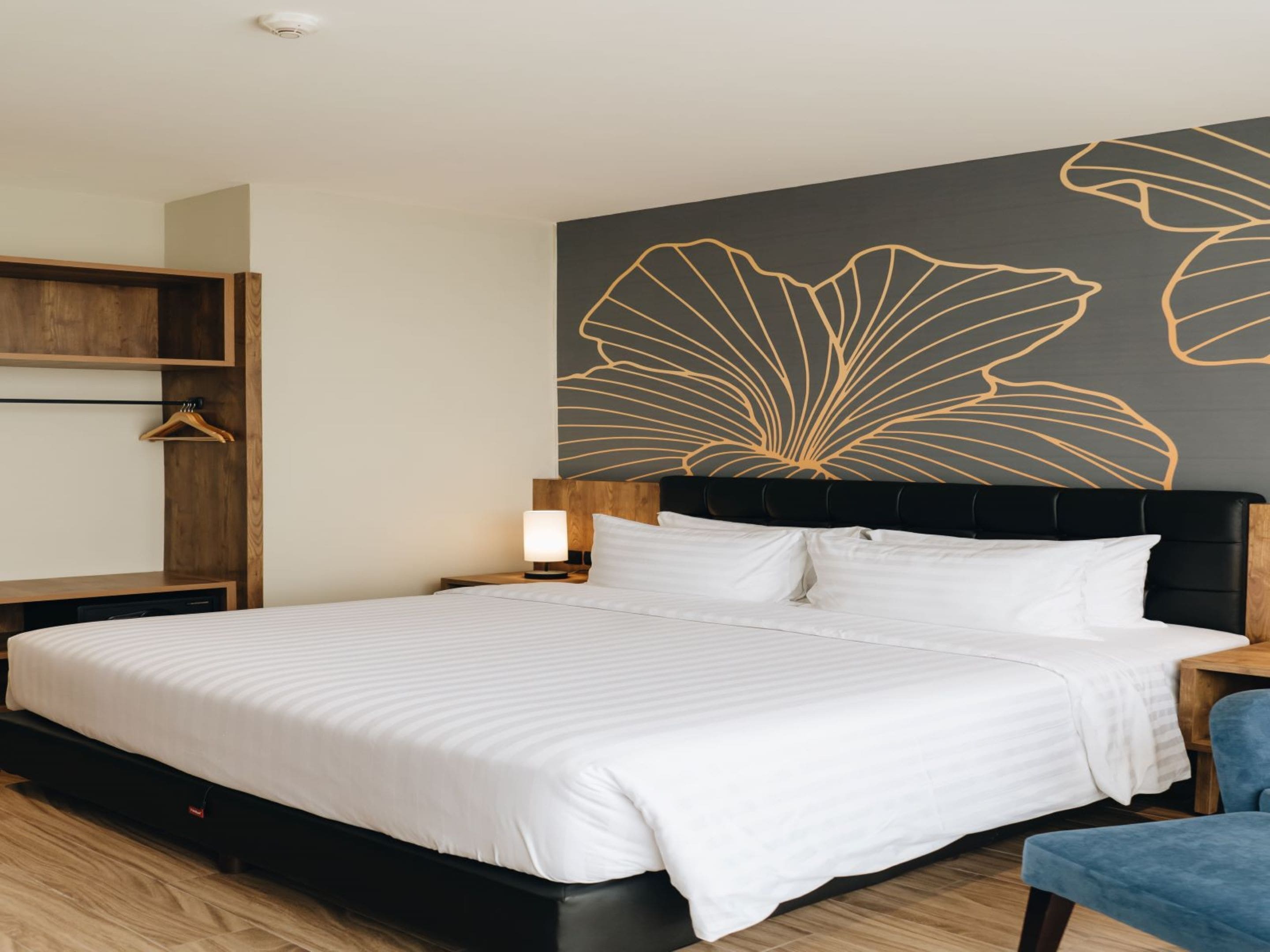 A neatly made bed with white linens, a black headboard, and a wall art of abstract leaf patterns.