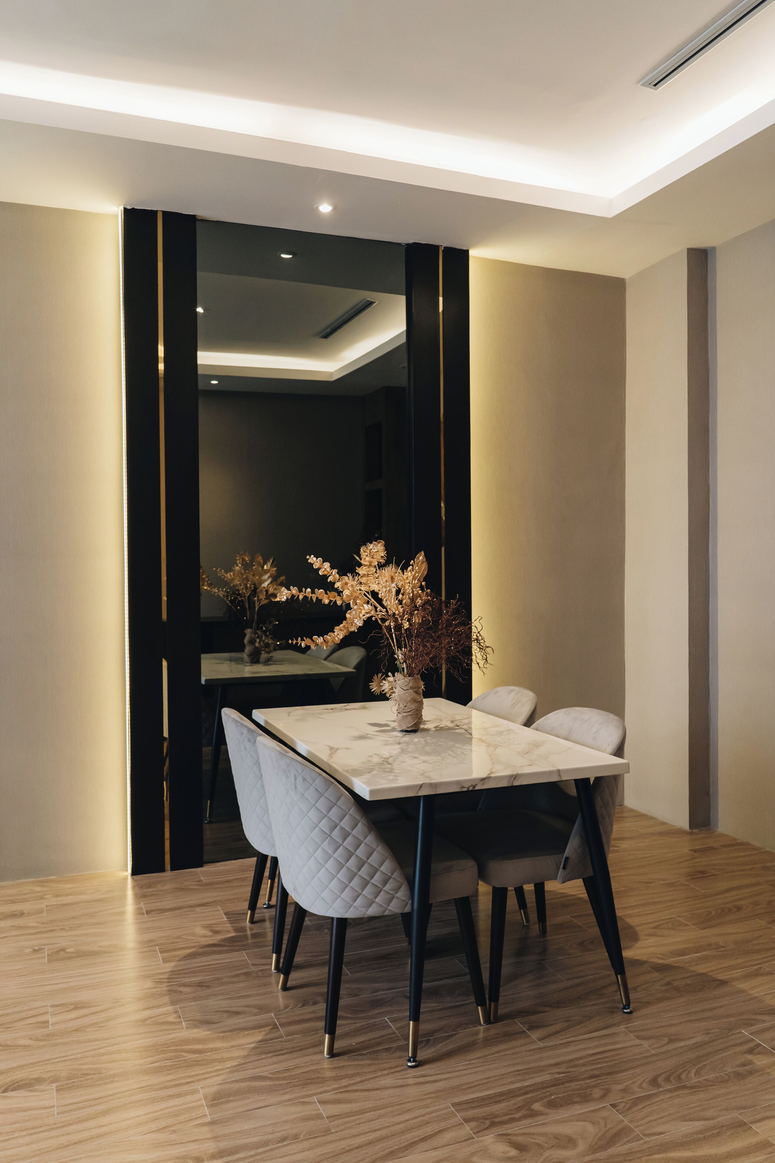 Un comedor moderno con una mesa de mármol, sillas acolchadas y un jarrón con flores secas.