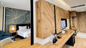 Et moderne hotelværelse med skrivebord i træ, seng, fjernsyn og et stort spejl.