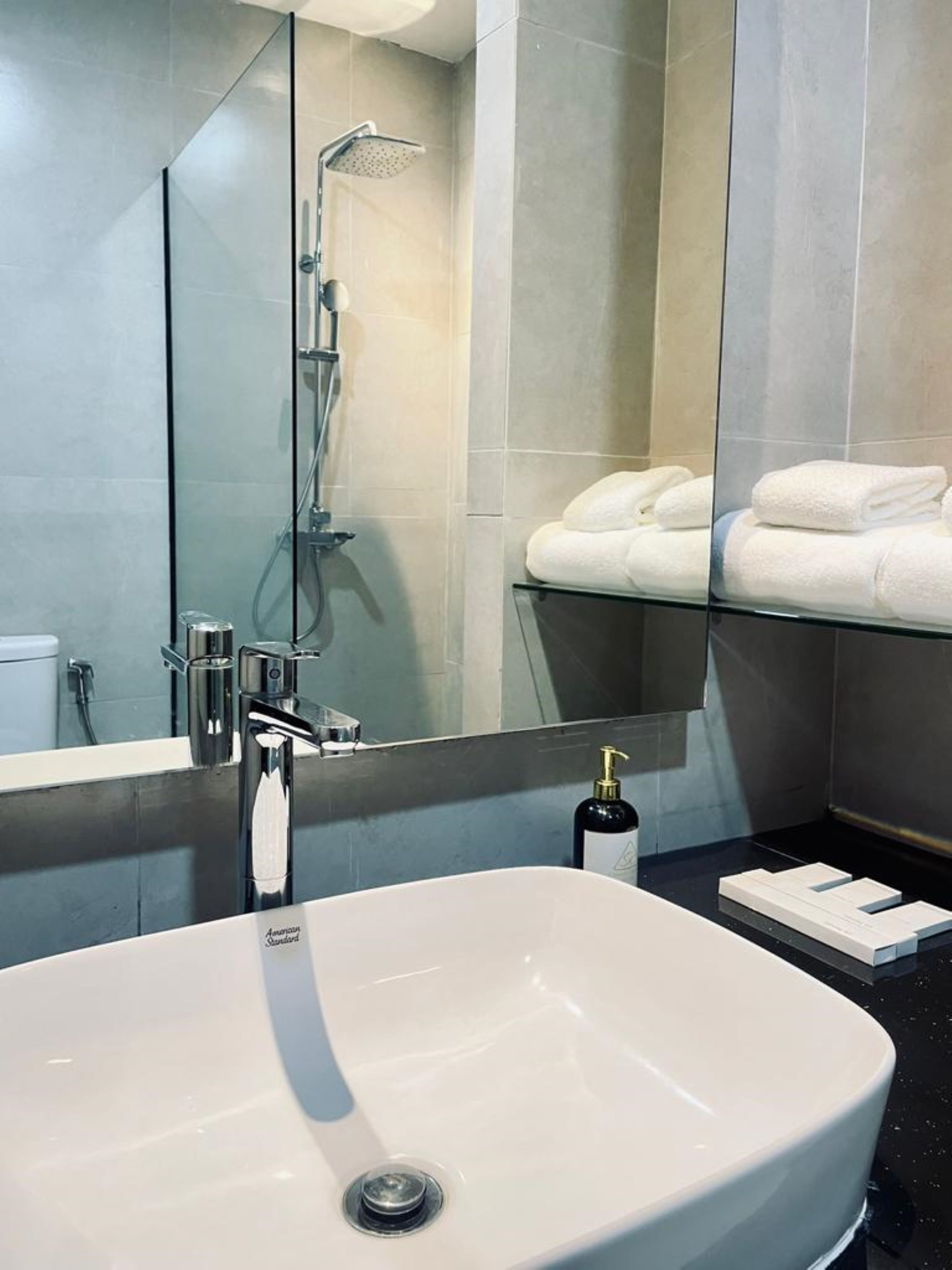 Un baño moderno con un lavamanos grande blanco, cabina de ducha de cristal y toallas blancas ordenadas en un estante.