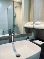 Un baño moderno con un lavamanos grande blanco, cabina de ducha de cristal y toallas blancas ordenadas en un estante.