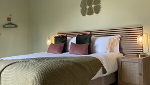 Ein ordentlich gemachtes Bett mit grüner Decke, einem Holz-Kopfstück und Nachttischlampen.