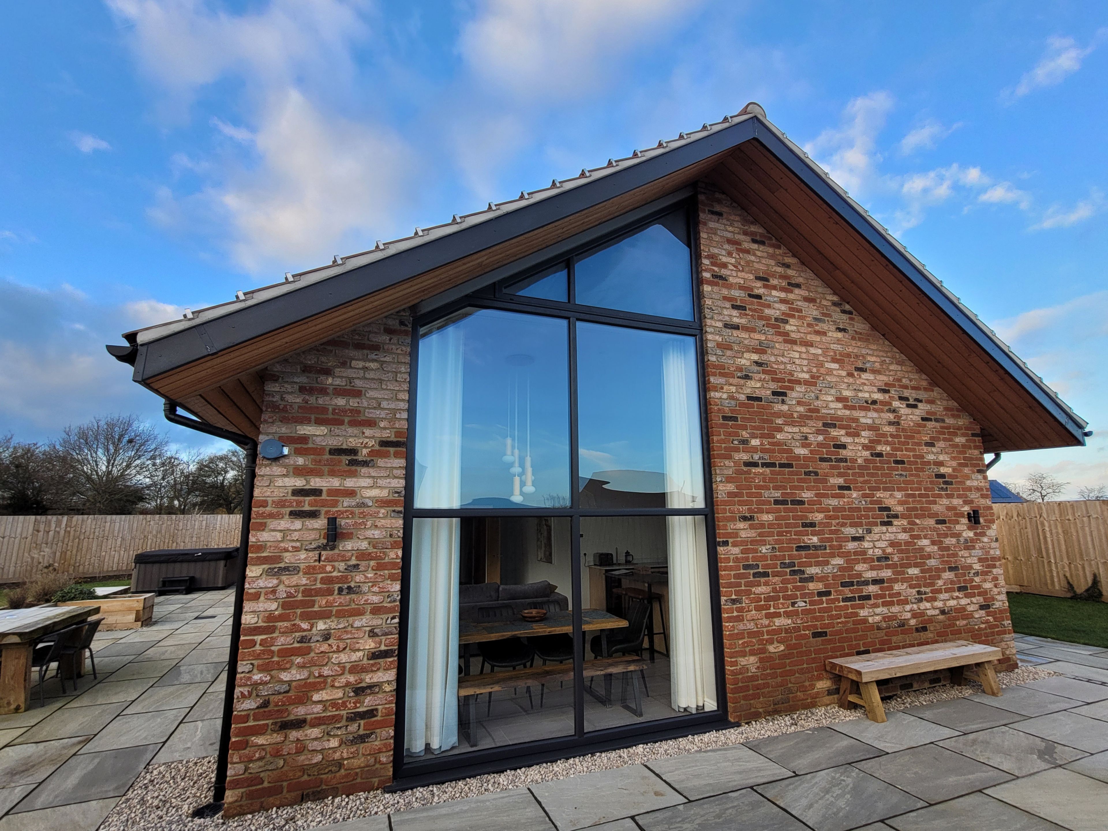 Ein modernes Haus mit einem großen Glasfenster, Ziegelmauern und einer Holzterrasse.