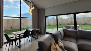 Ein modernes Wohnzimmer mit großem Fenster, Essbereich und Blick auf den Garten.