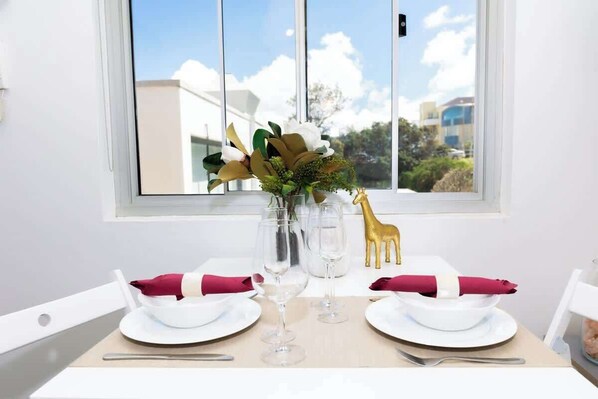 A dining table set with white plates, red napkins, and clear glasses, with a vase of flowers and a golden giraffe decoration.