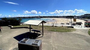 A beachside view with a covered picnic area, a parking lot, and a view of the beach and ocean. - Cozy beachfront studio with aircon (North Bondi)