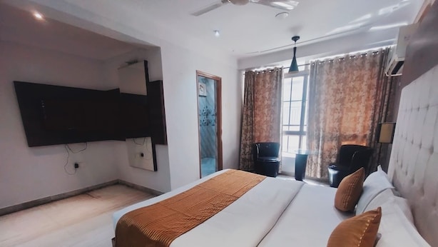 A hotel room with a large bed, a flat-screen TV mounted on the wall, a ceiling fan, and a window with curtains. - Heterosis (Udaipur)