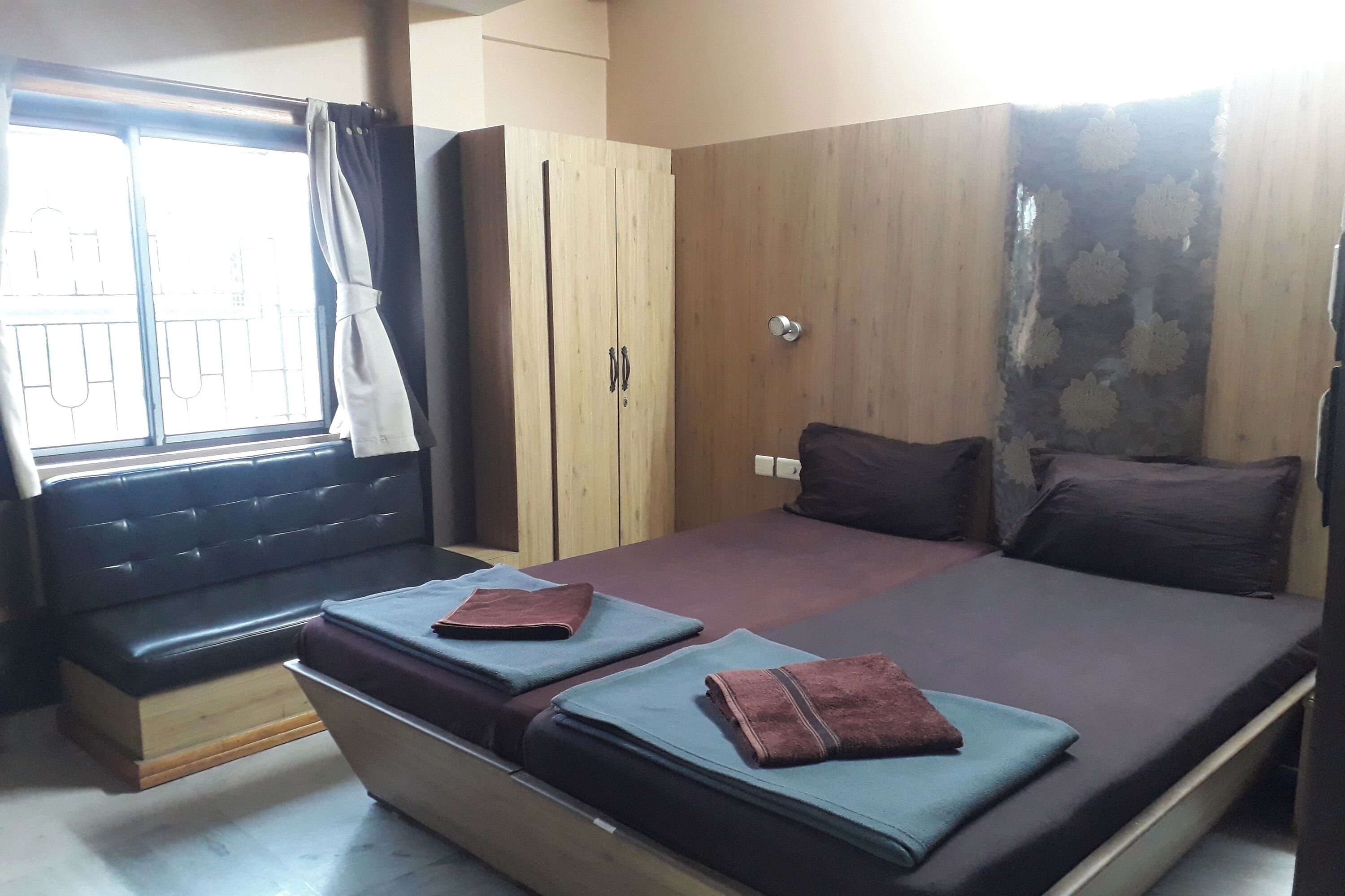 A room with a bed, a bench, a wardrobe, and a window with curtains.