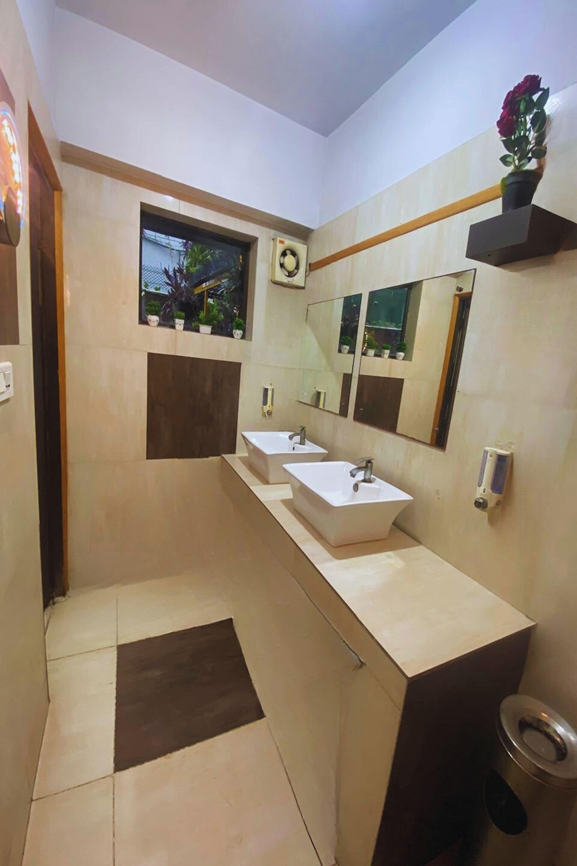 A modern bathroom with two sinks, a window with a view of plants, and a mirror above the sinks.