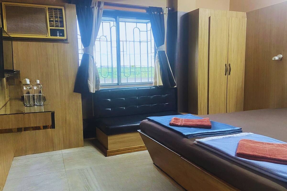 A compact room with a bed, a small table with glasses, a window with curtains, and a wardrobe.