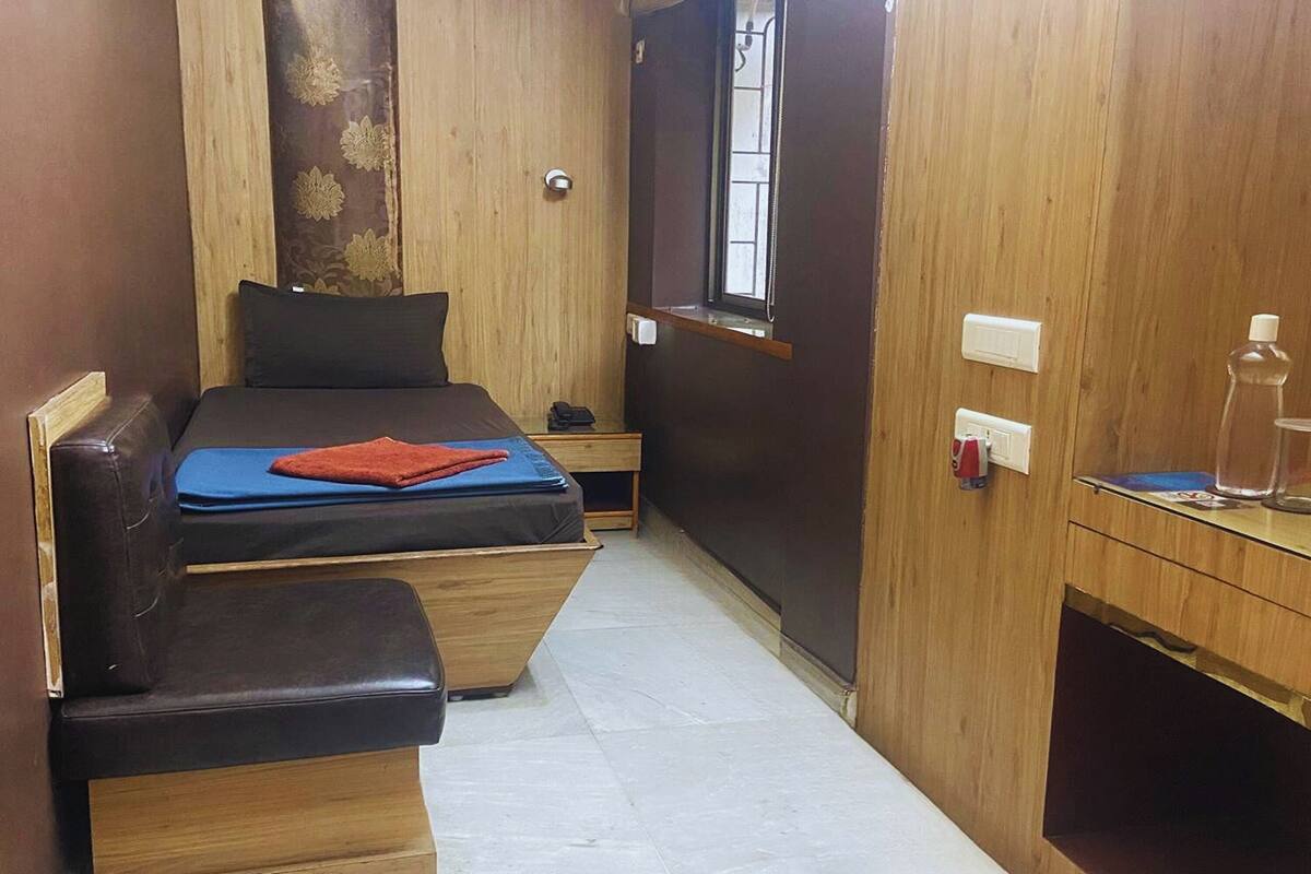 A compact room with a bed, a bench, a small table, and a window.