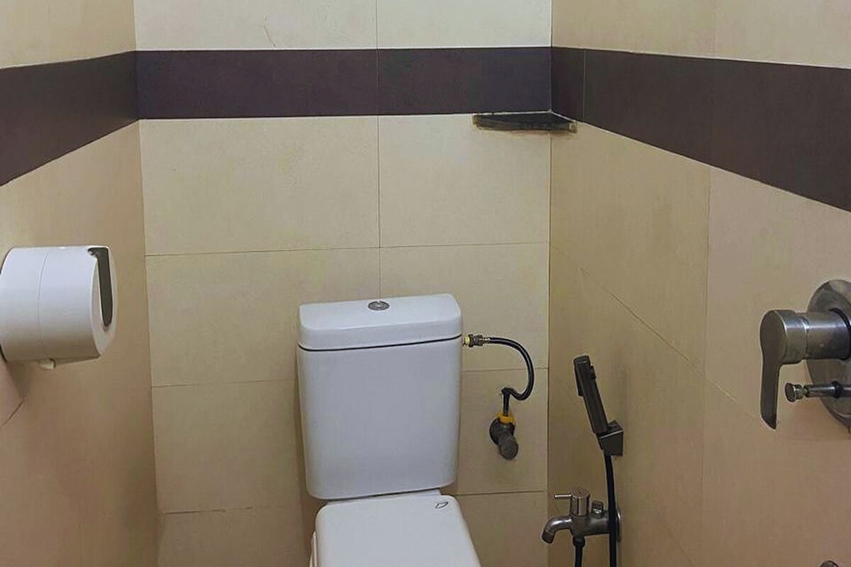 A small, tiled bathroom with a toilet, a hand dryer, and a showerhead.