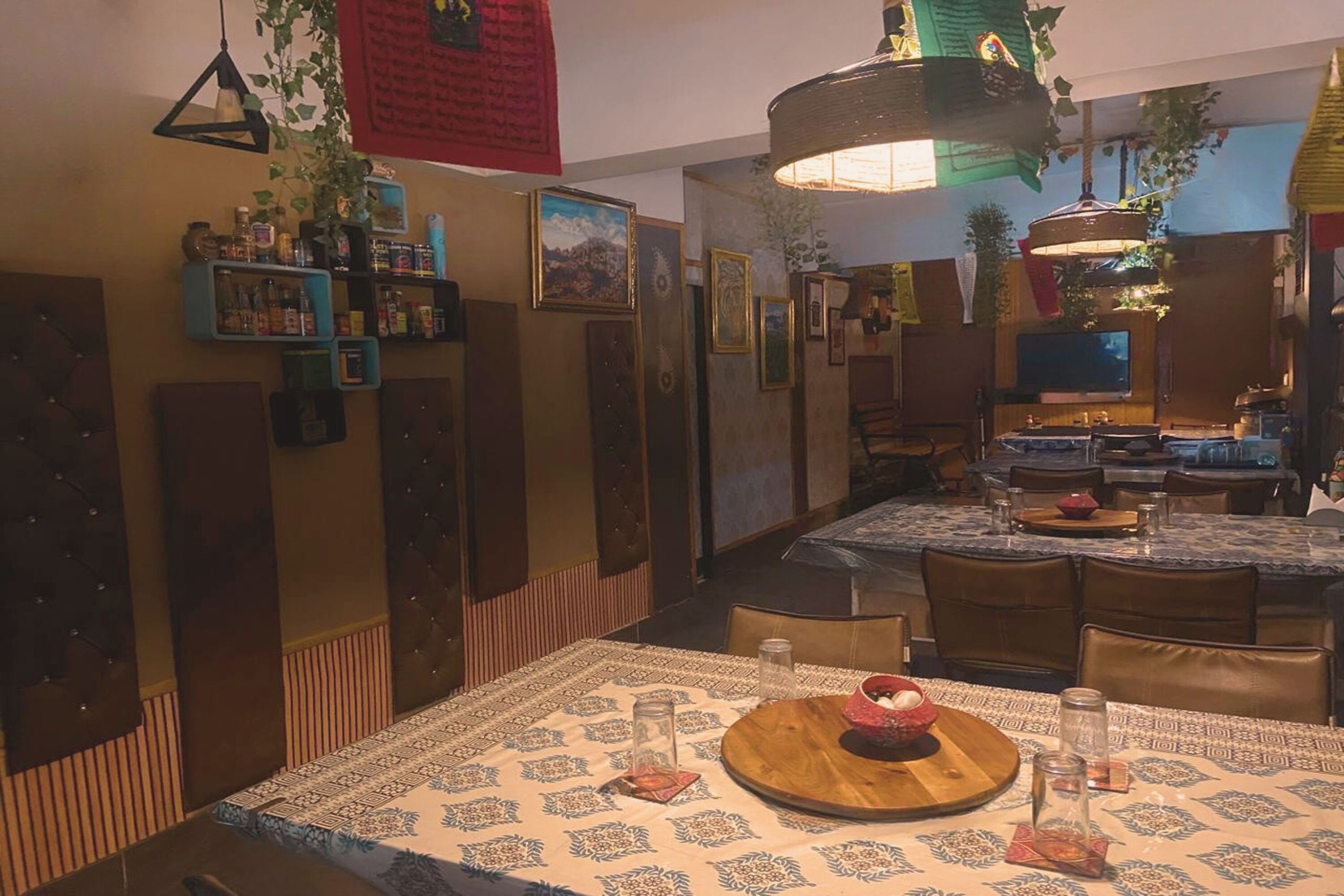 Un restaurante acogedor con una larga mesa de comedor, sillas, y una variedad de plantas colgantes y adornos.