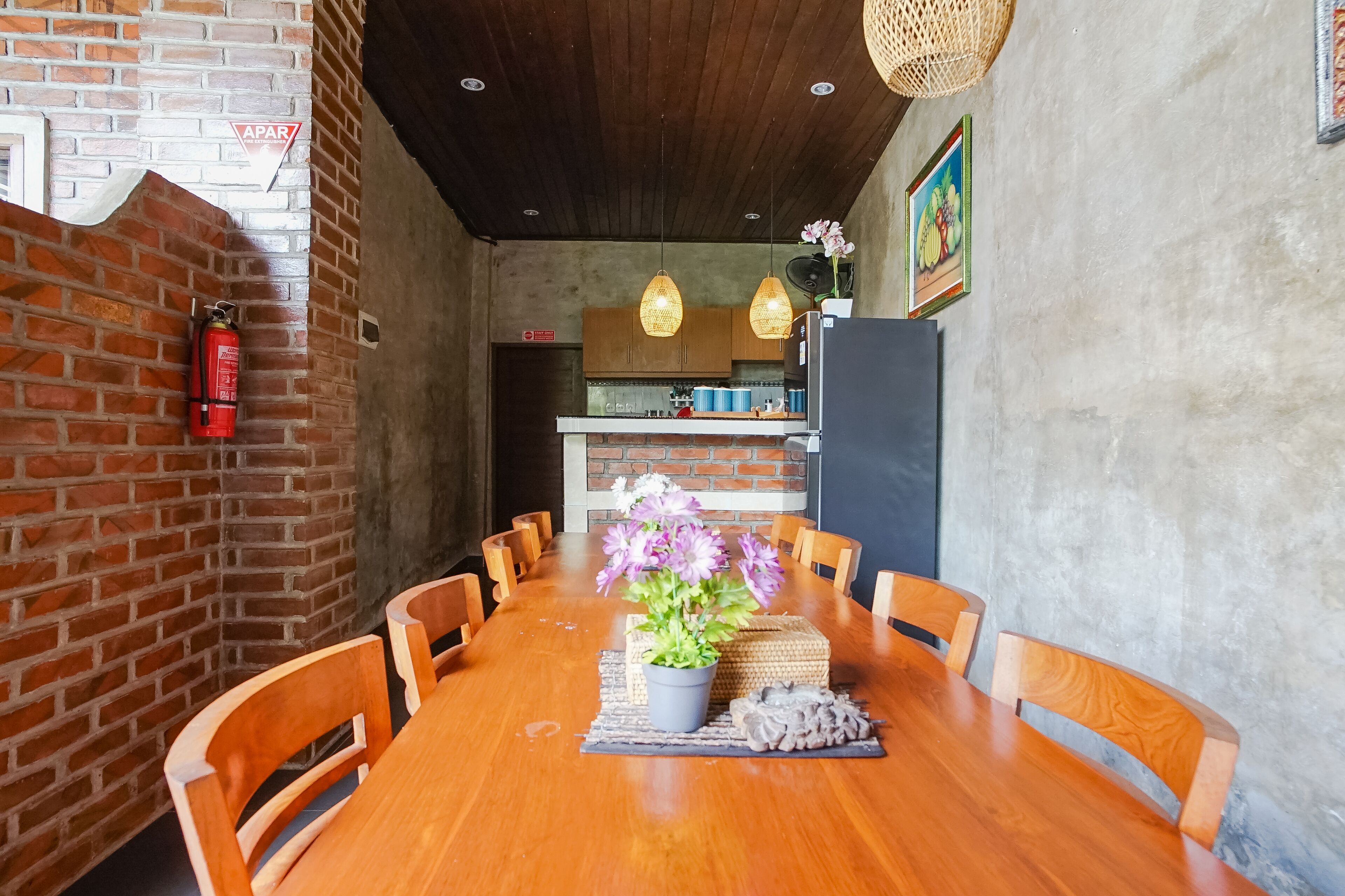 A wooden dining table with chairs, a potted plant, and a fire extinguisher on the wall.