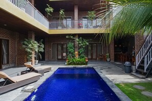 A pool area with lounge chairs, a brick building, and a balcony. - D'Meten Guest House Canggu (Canggu)