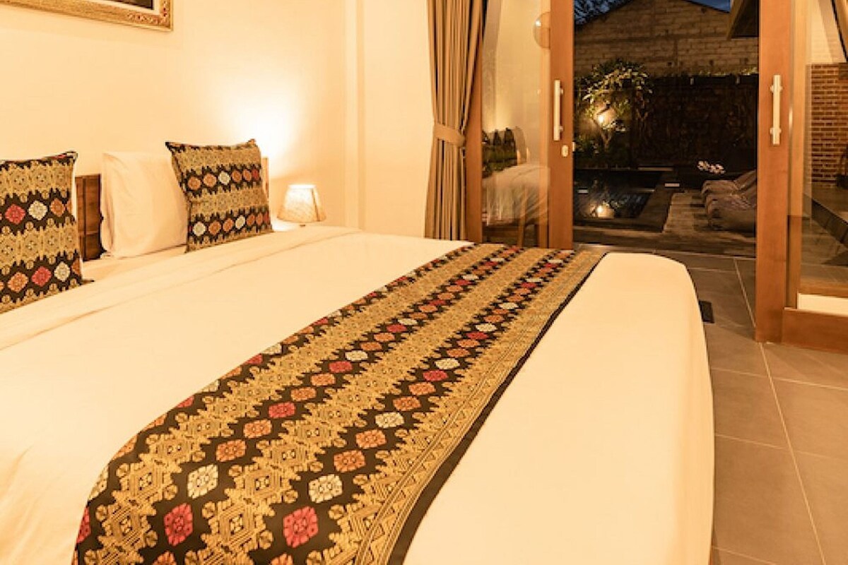 A hotel room with a large bed, a painting on the wall, and a sliding glass door leading to an outdoor area.