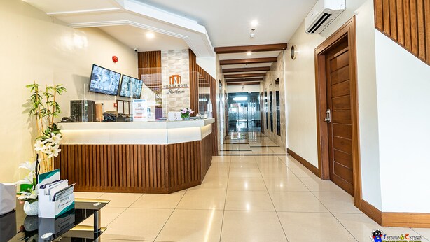 A hotel reception area with a wooden reception desk, multiple monitors, and a clean, tiled floor. - Verjandel Residences (Quezon City)