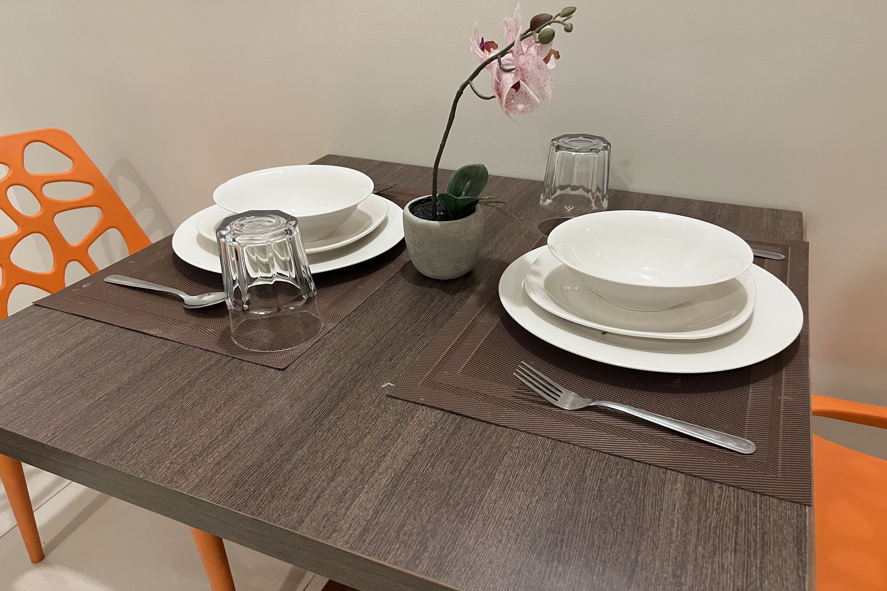 A dining table set with white plates, a clear glass, a small potted plant, and a fork.