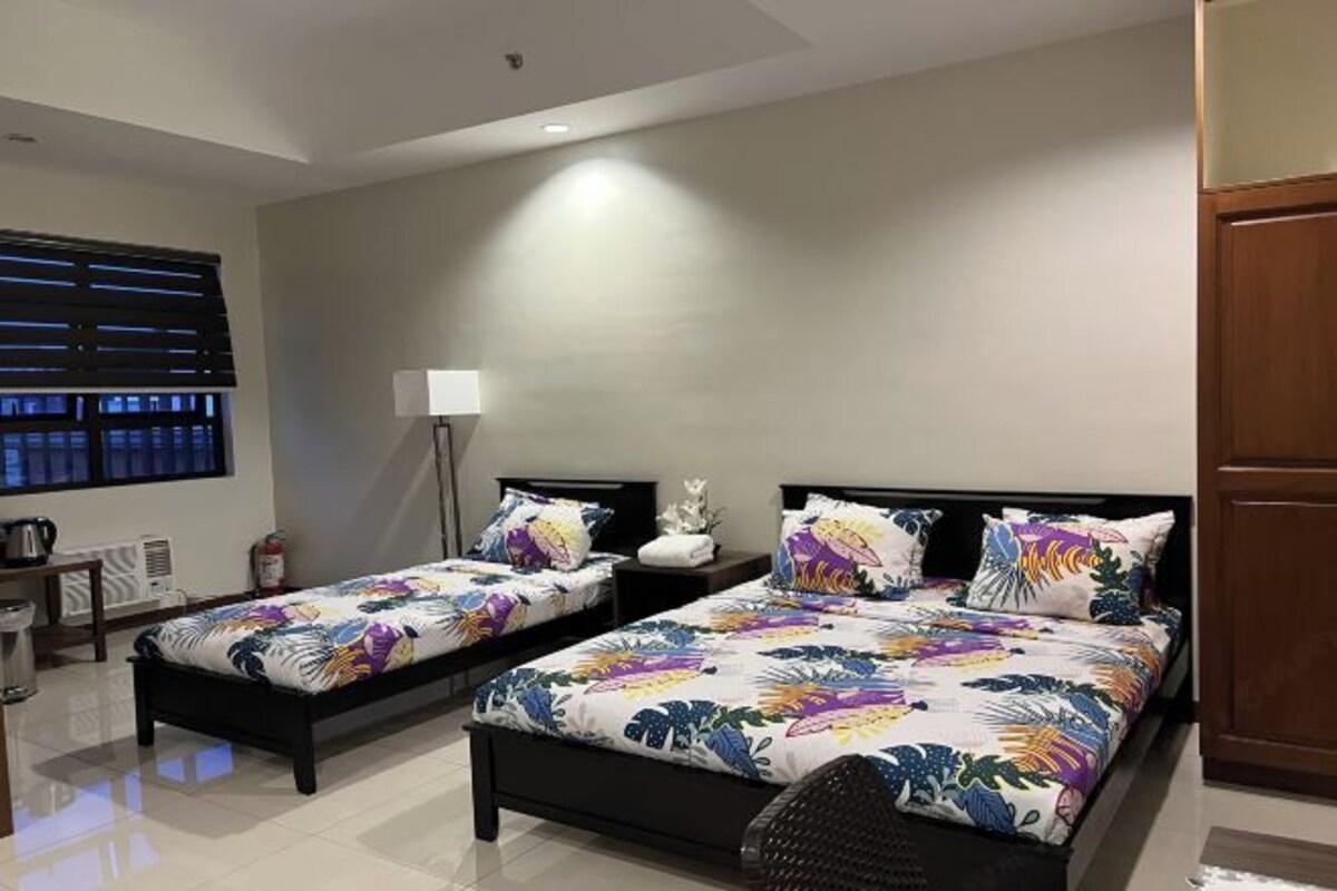 A hotel room with two beds, a desk, a chair, a lamp, and a window with blinds.
