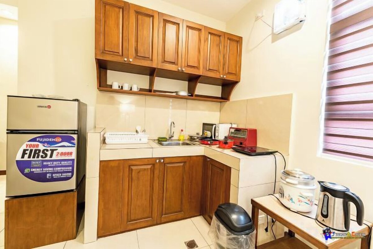 A compact kitchen with wooden cabinets, a refrigerator, a kettle, and a small table.