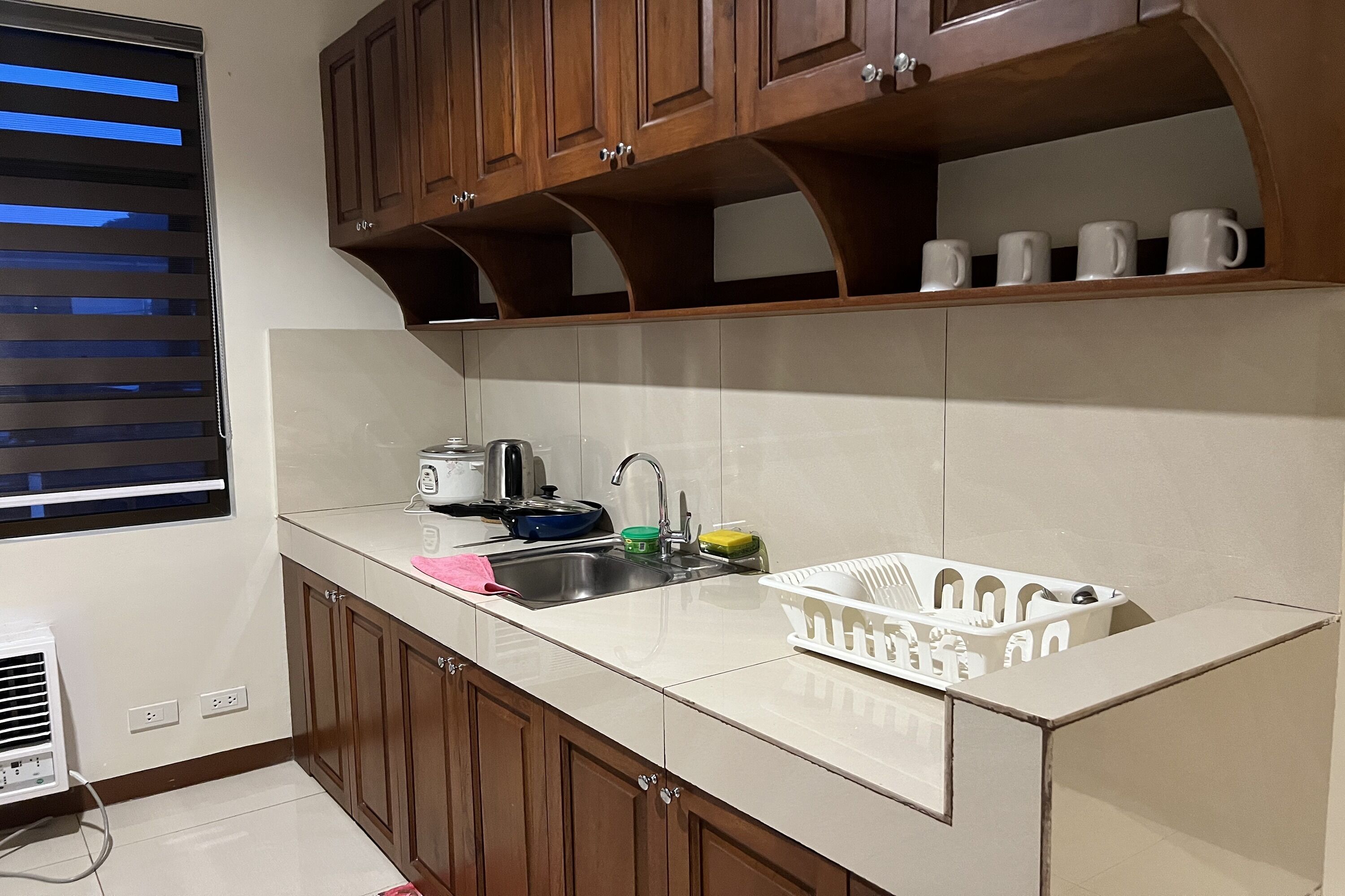 A kitchen with wooden cabinets, a white countertop, a sink, a toaster, and a window with blinds.