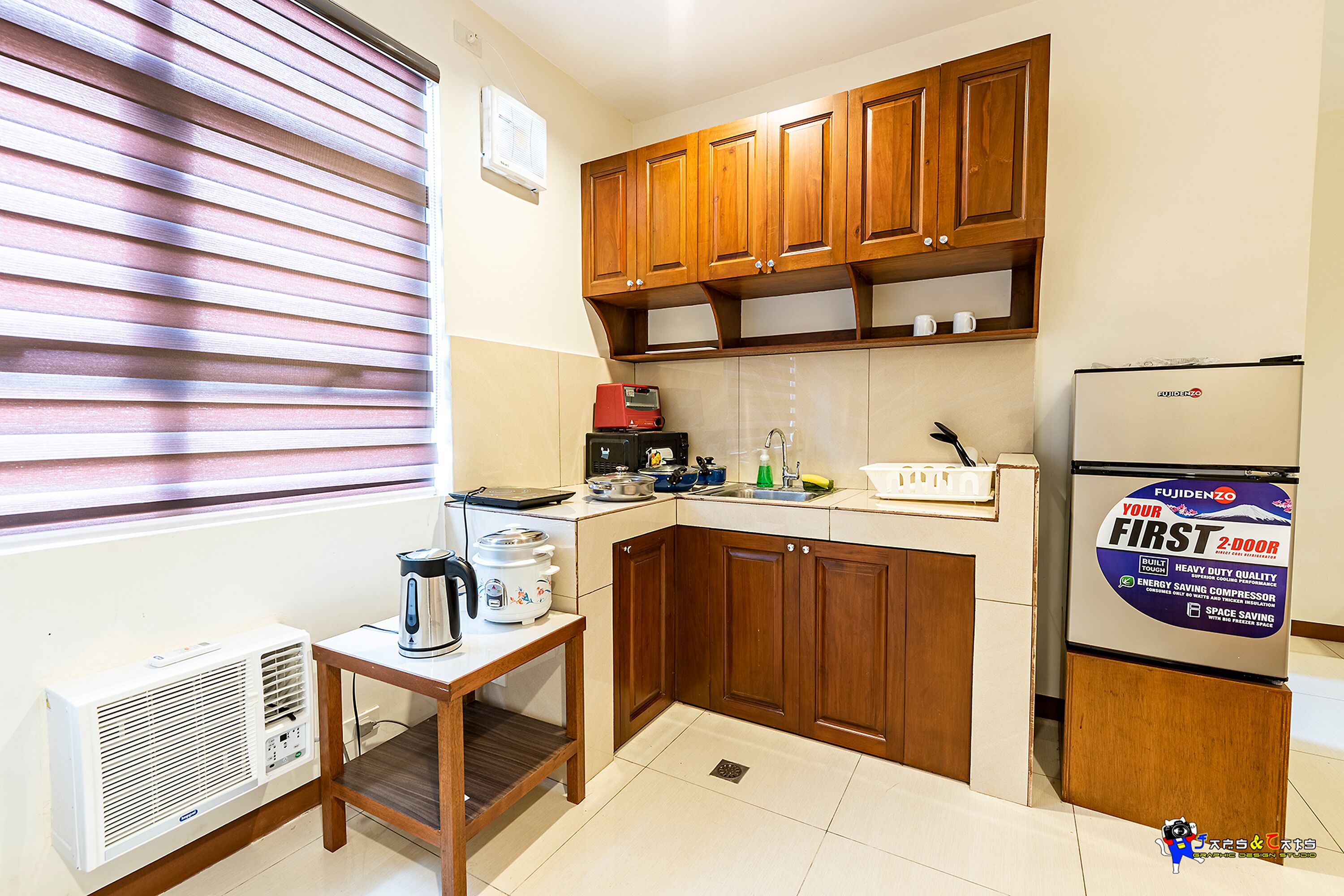 A compact kitchen with wooden cabinets, a built-in stove, and a refrigerator with a promotional sticker.